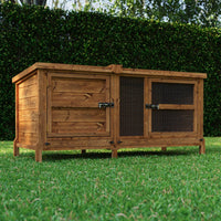 Wooden rabbit hutch on grass with greenery in the background