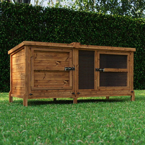 Wooden rabbit hutch on grass with greenery in the background