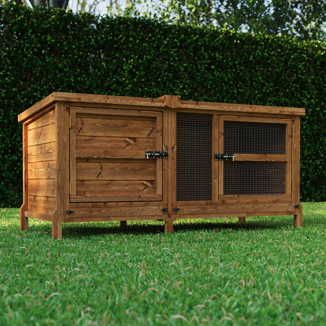 Wooden rabbit hutch on grass with greenery in the background