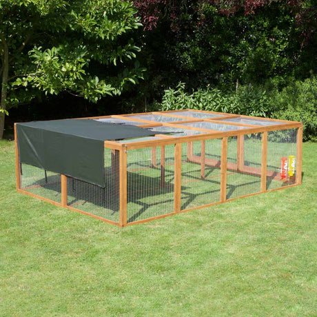 Wooden rabbit run with a green cover on grass with trees in the background