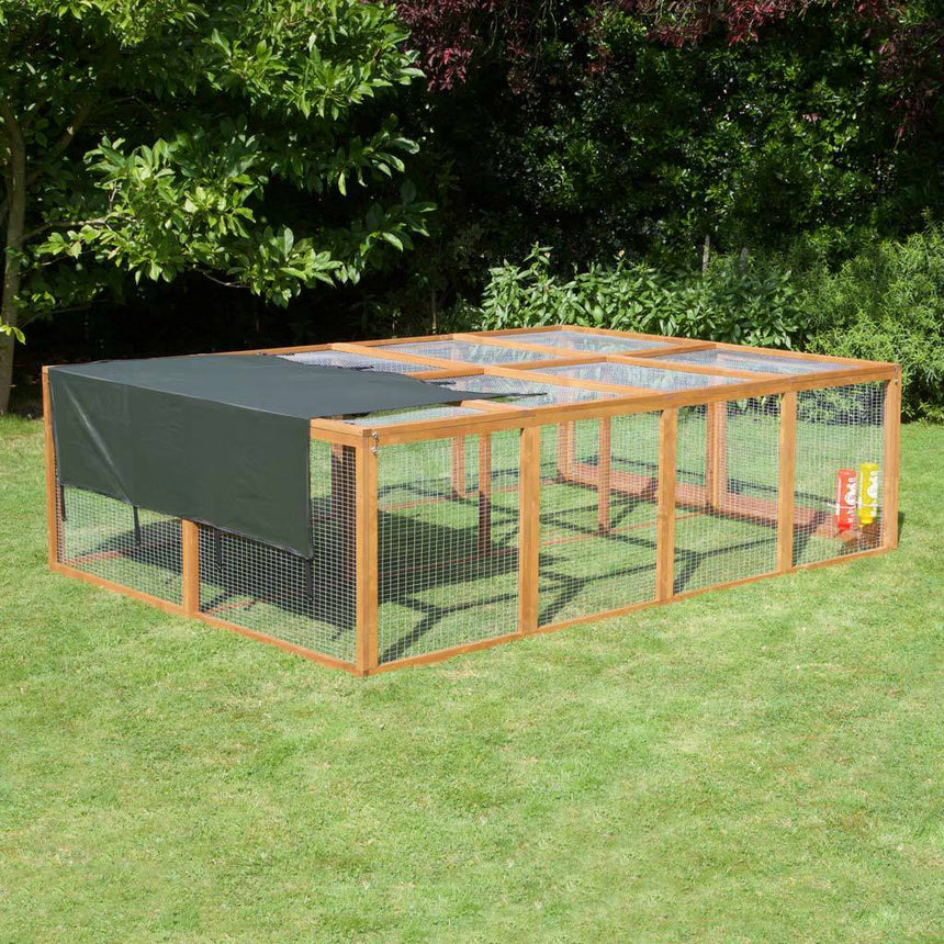 Wooden rabbit run with a green cover on grass with trees in the background