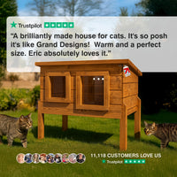 Wooden cat house with two cats in a garden, featuring Trustpilot review text. “A brilliantly made house for cats. It's so posh it's like Grand Designs!  Warm and a perfect size. Eric absolutely loves it.”