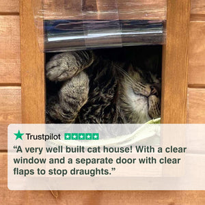 Cat peeking out from a wooden cat house with a clear window and flaps. “A very well-built cat house! With a clear window and a separate door with clear flaps to stop draughts.”