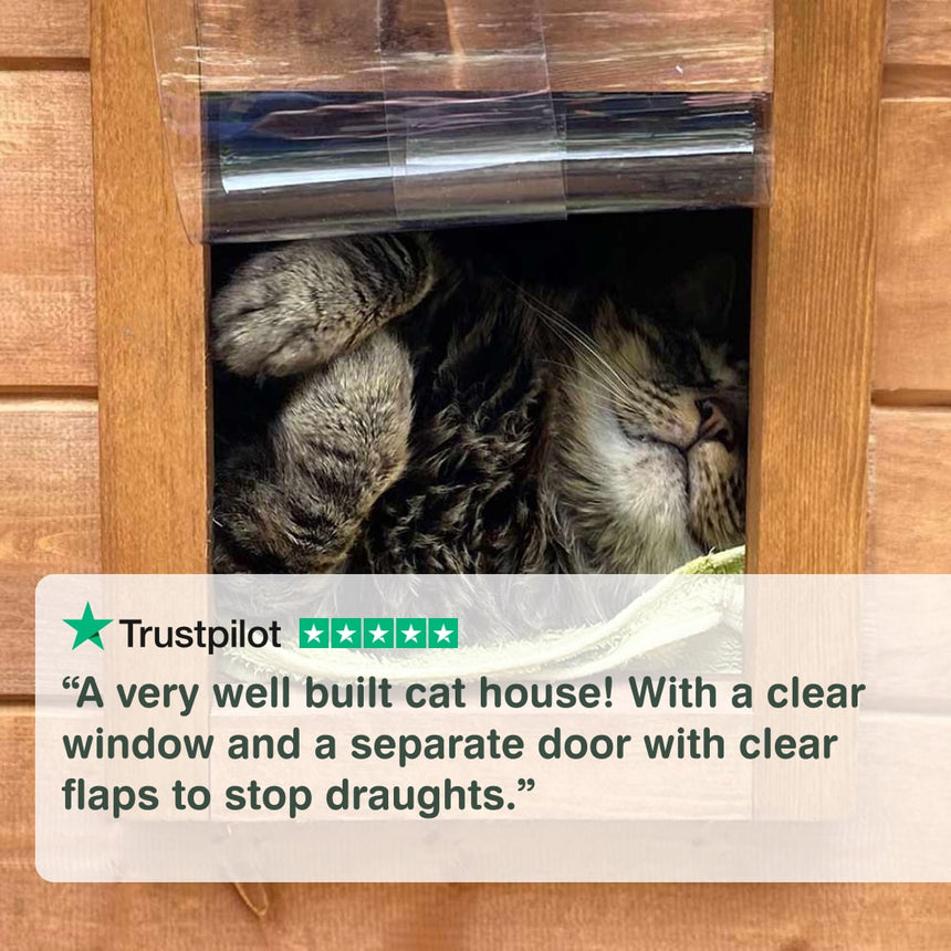 Cat peeking out from a wooden cat house with a clear window and flaps. “A very well-built cat house! With a clear window and a separate door with clear flaps to stop draughts.”